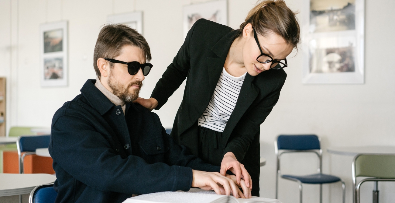 Pessoa cega a ler braille com a ajuda de outra pessoa