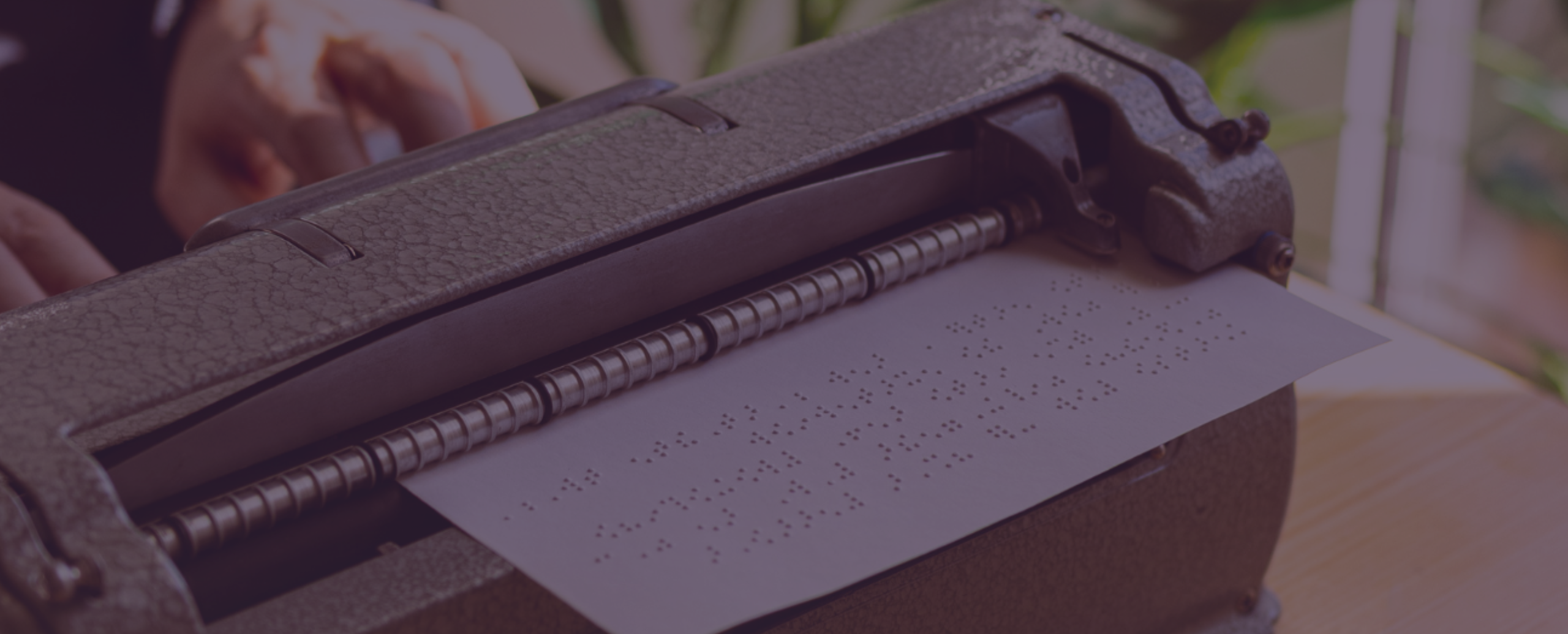 Máquina de escrever Braille com uma folha de papel contendo texto em Braille.