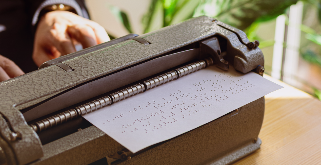 Máquina de escrever Braille com uma folha de papel contendo texto em Braille.